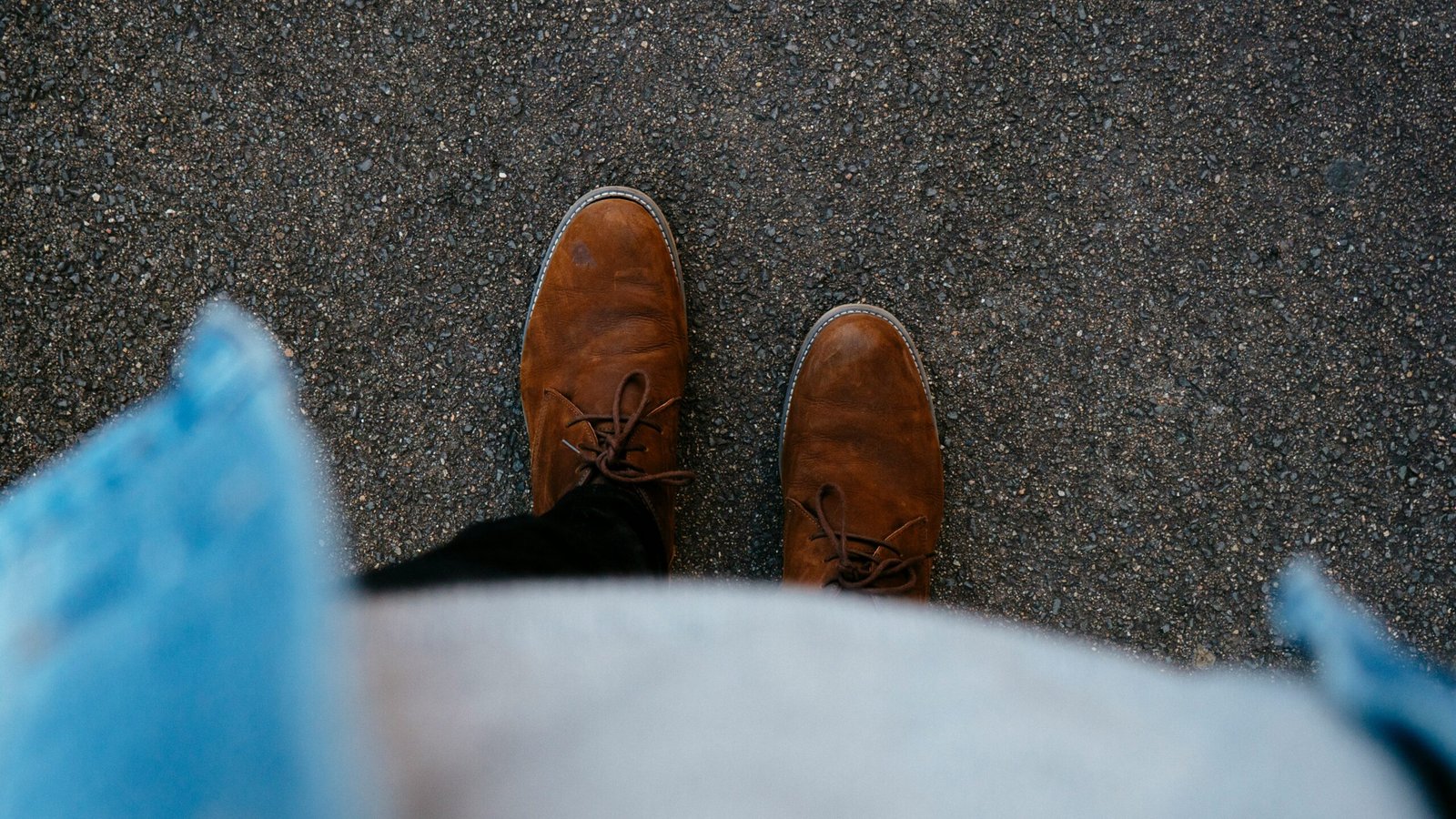 person wearing pair of brown leather boots standing on asphalt surface